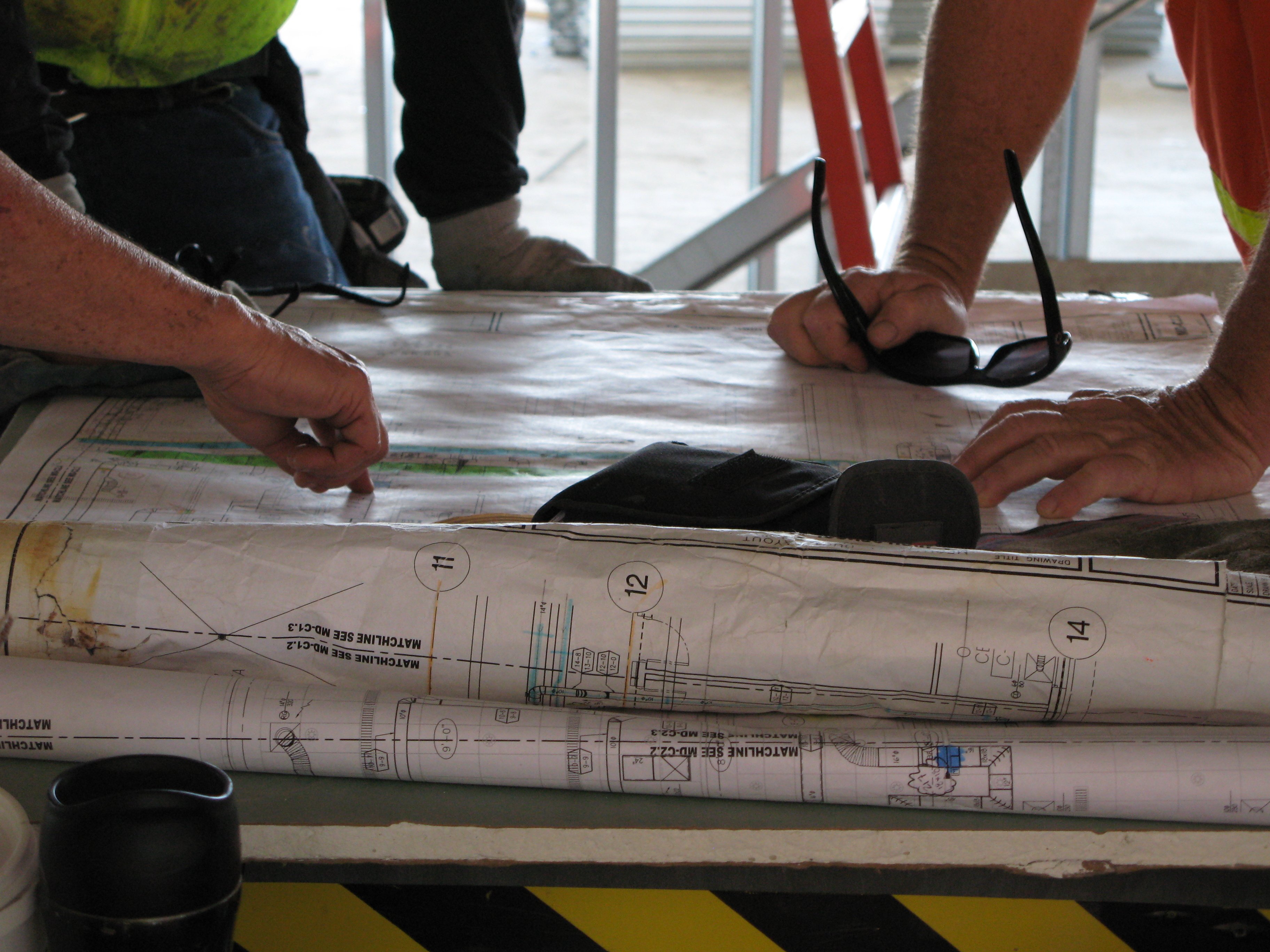 Hands of trade workers and an Athena Engineering project manager reviewing plans together on a jobsite.